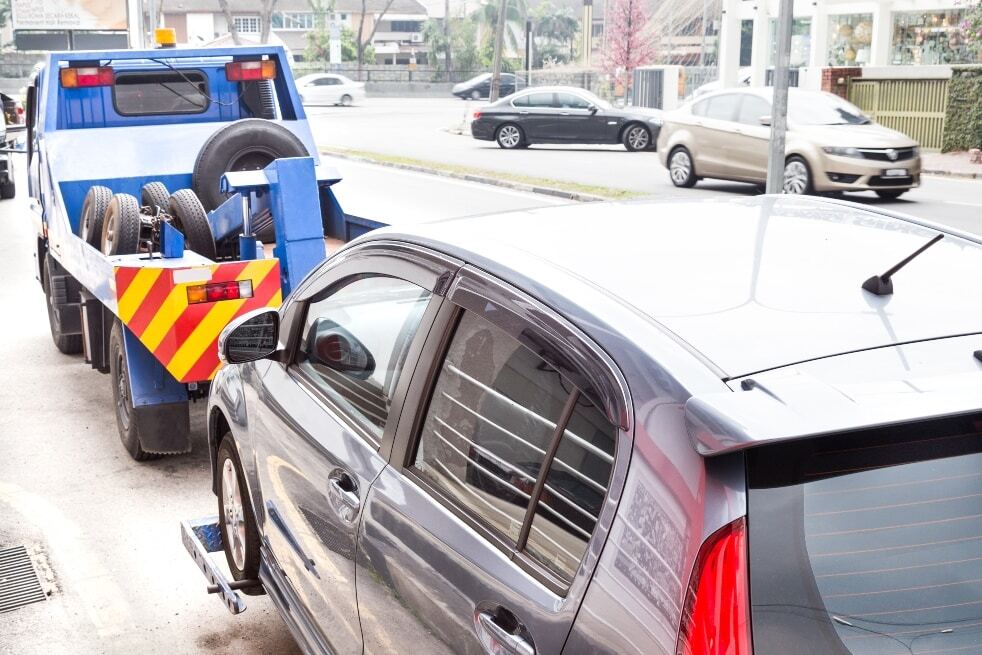 Tow truck towing a broken down car on the street.