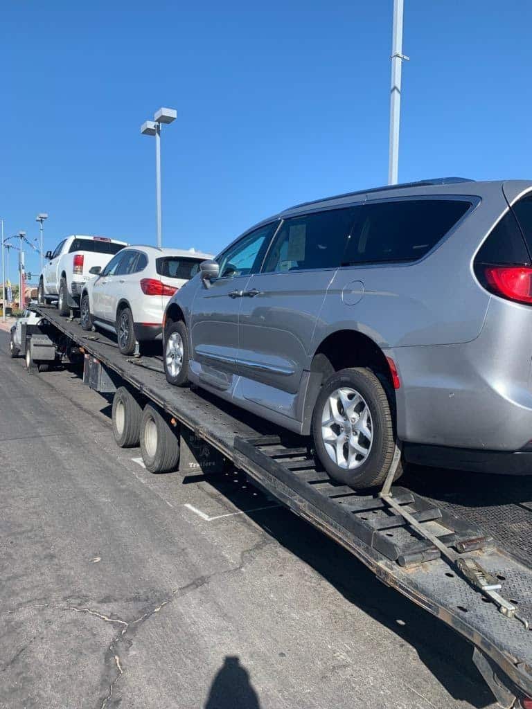 Several vehicles, including a gray minivan, on a car carrier trailer under a blue sky.