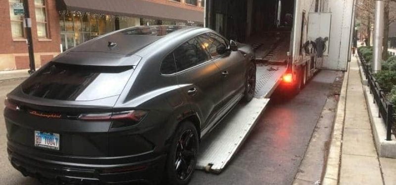 black lamborgini suv loading into enclosed transport trailer on busy street