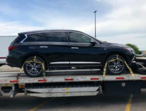 Infiniti JX35 strapped to transport trailer in parkling lot