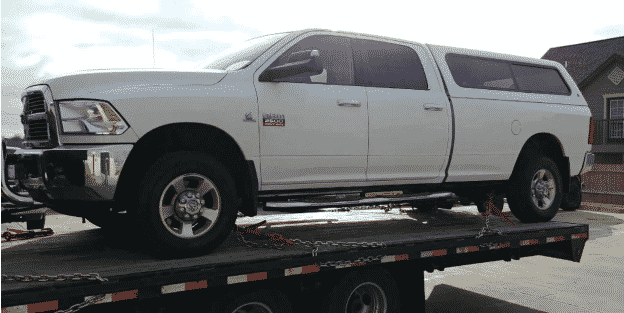 White Ram 2500 truck secured to a flatbed trailer.
