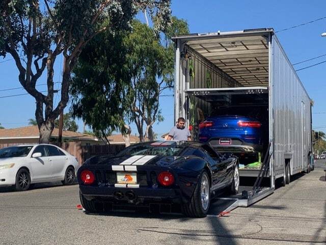 Black Ford GT with white racing stripes on a car hauling trailer, with a blue car above.