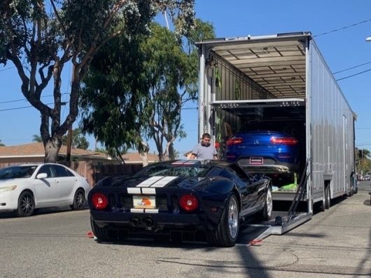 Black Ford GT with white racing stripes on a car hauling trailer, with a blue car above.