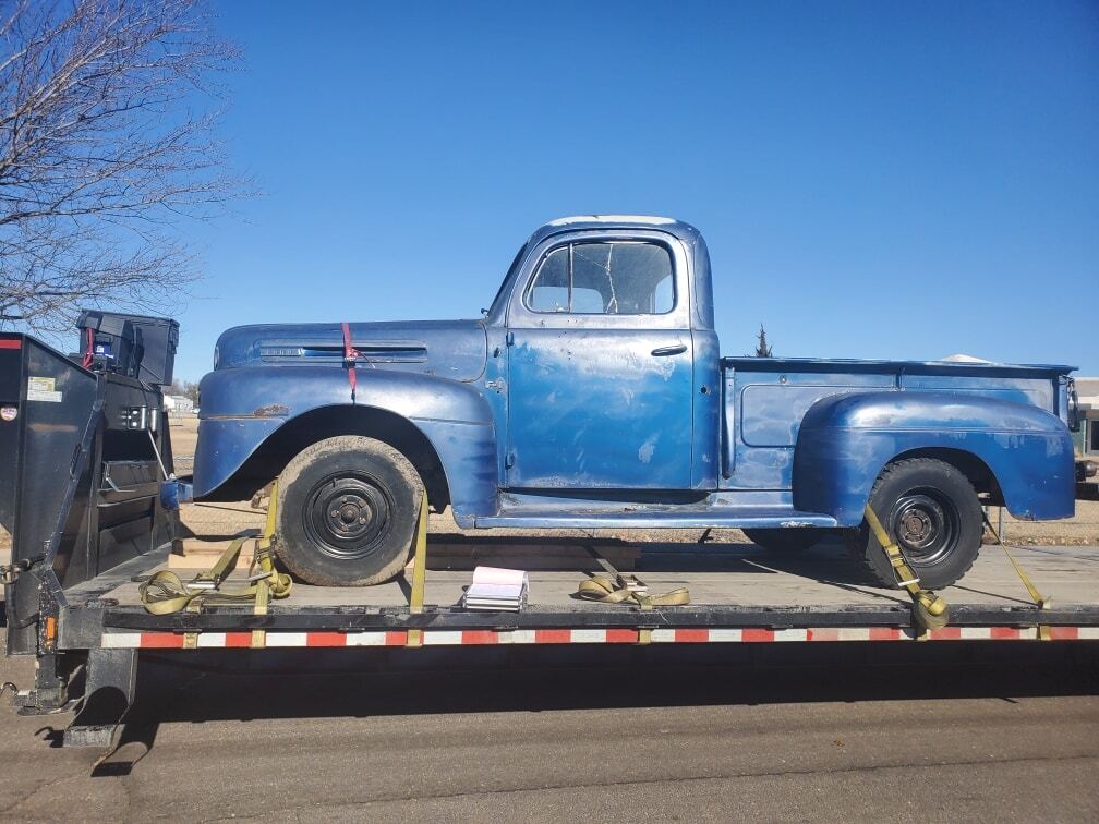 Vintage light-blue Ford pickup truck strapped onto a trailer.