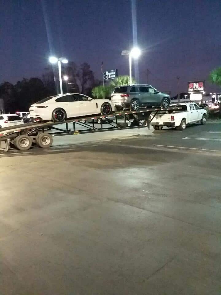 A car carrier on the street transporting a white car and an SUV.