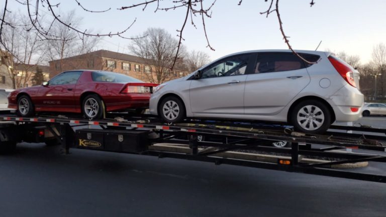 Red Chevrolet Camaro IROC Z and silver Hyundai Accent being transported on a black Kaufman trailer.
