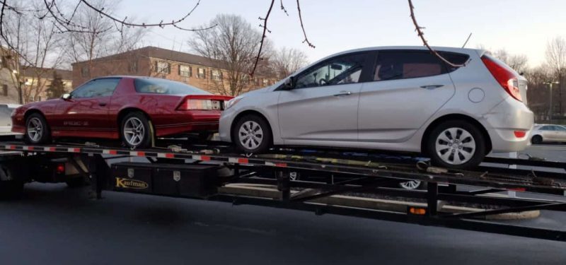 Red Chevrolet Camaro IROC Z and silver Hyundai Accent being transported on a black Kaufman trailer.
