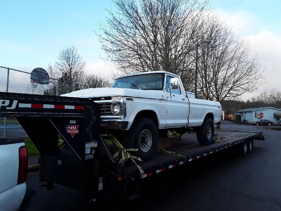 White vintage pickup truck strapped to a black PJ trailer.
