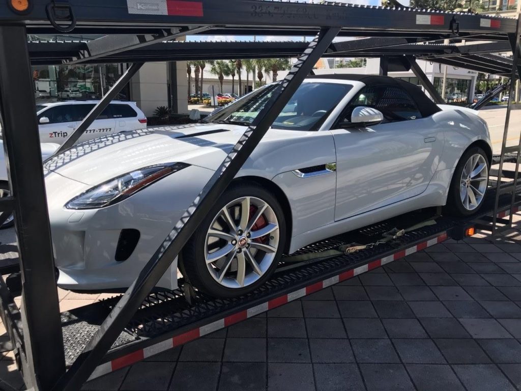 A white Jaguar F-Type convertible is strapped to a car carrier.