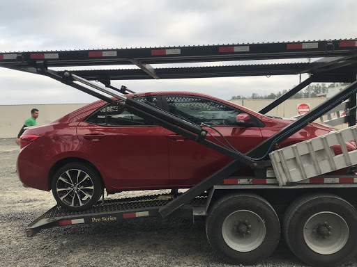 A red Toyota Prius on a car carrier trailer, with a man standing in the background outdoors.