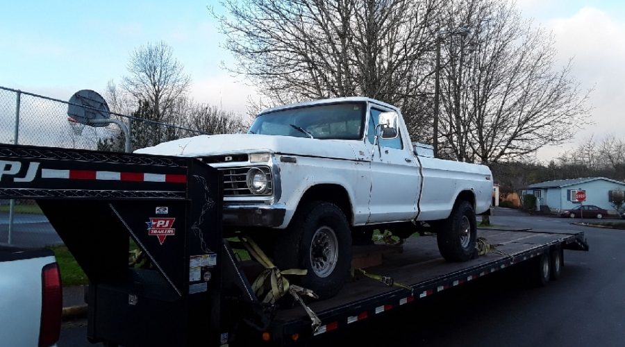White vintage pickup truck strapped to a black PJ trailer.