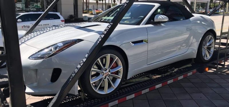 A white Jaguar F-Type convertible is strapped to a car carrier.