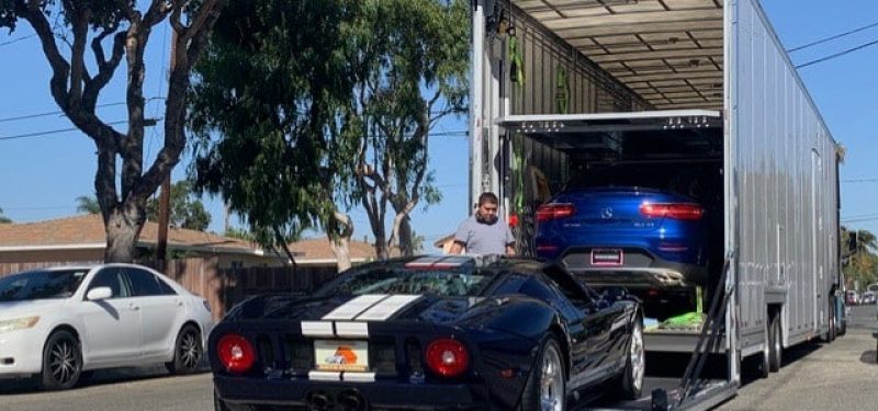 Black Ford GT with white racing stripes on a car hauling trailer, with a blue car above.