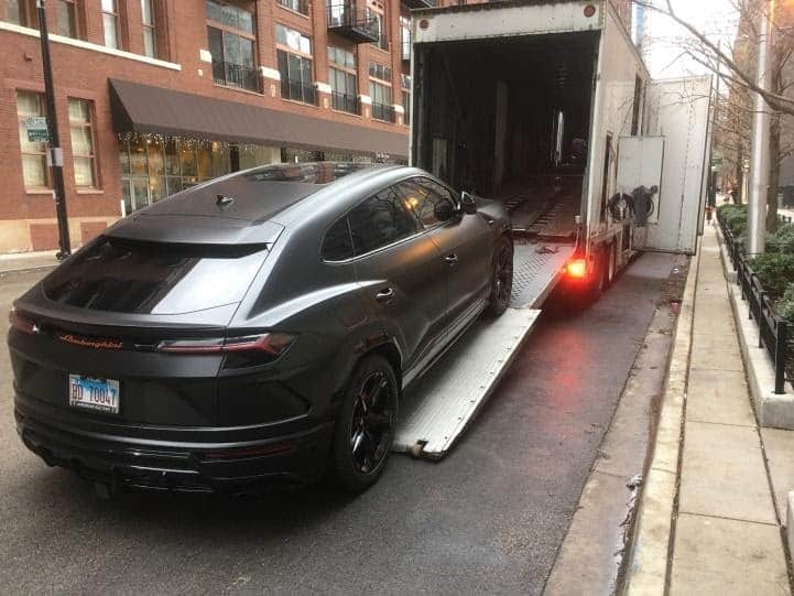 black lamborgini suv loading into enclosed transport trailer on busy street