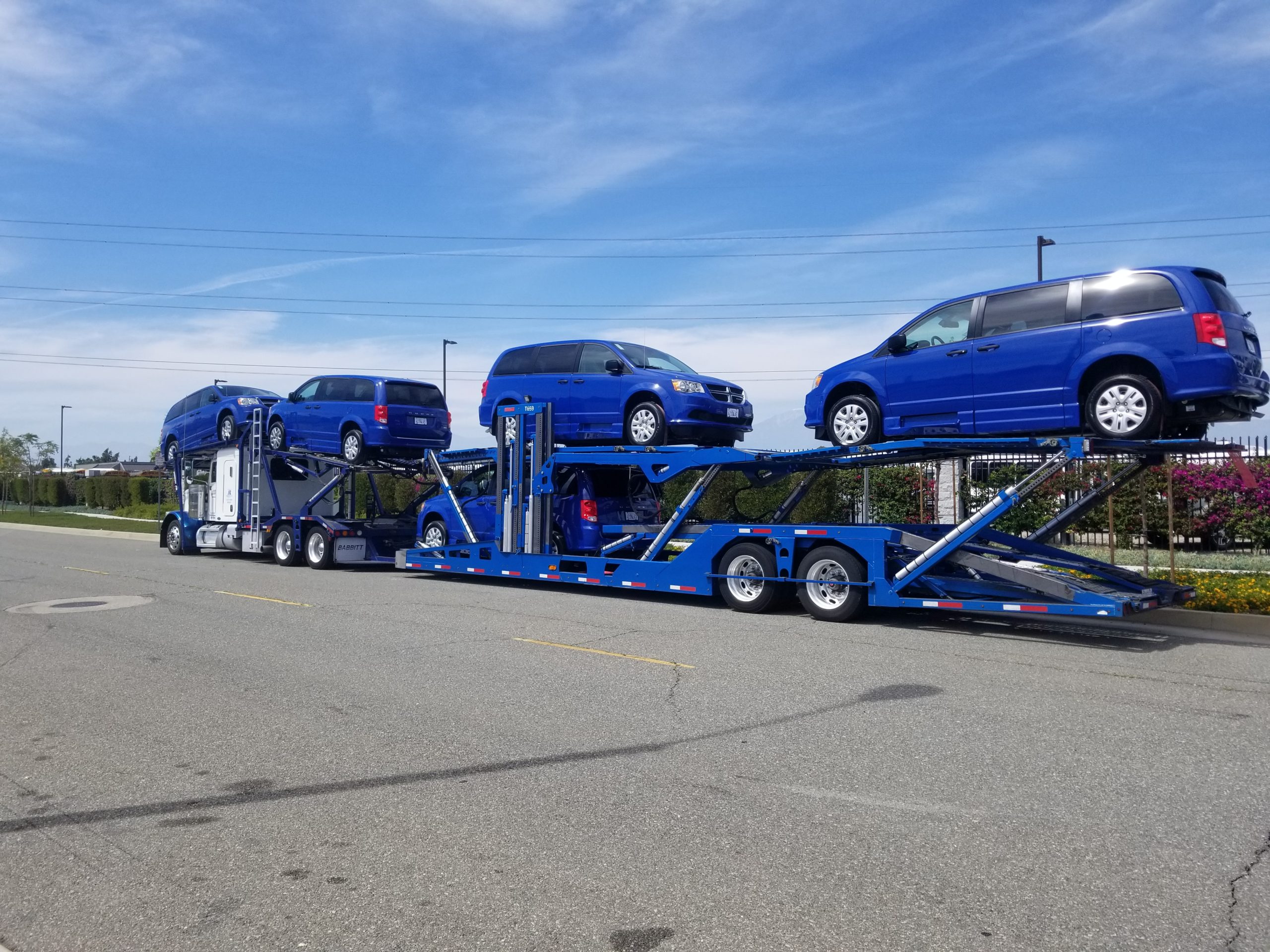 Four blue mobility vans on auto transport trailers on concrete road