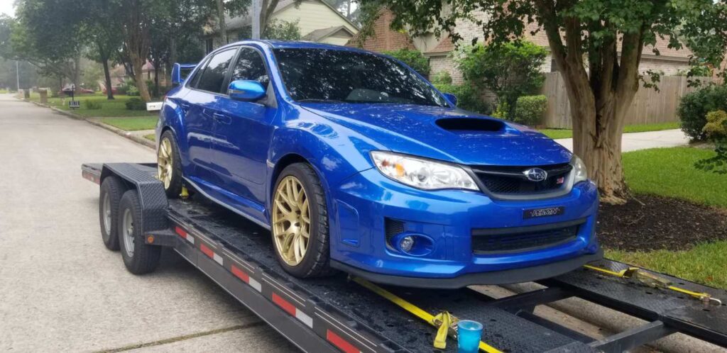 blue subaru sti car on trailer in neighborhood