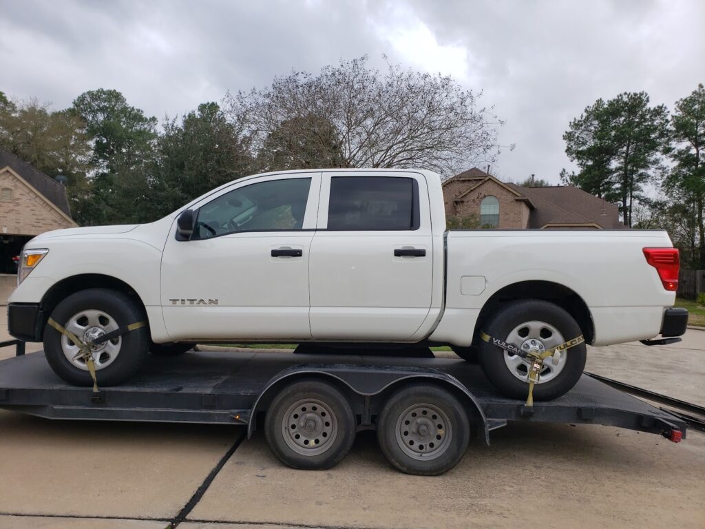 white nissan titan truck on transport trailer in residential driveway