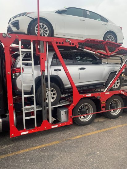 a red car transport trailer with two vehicles inside of it